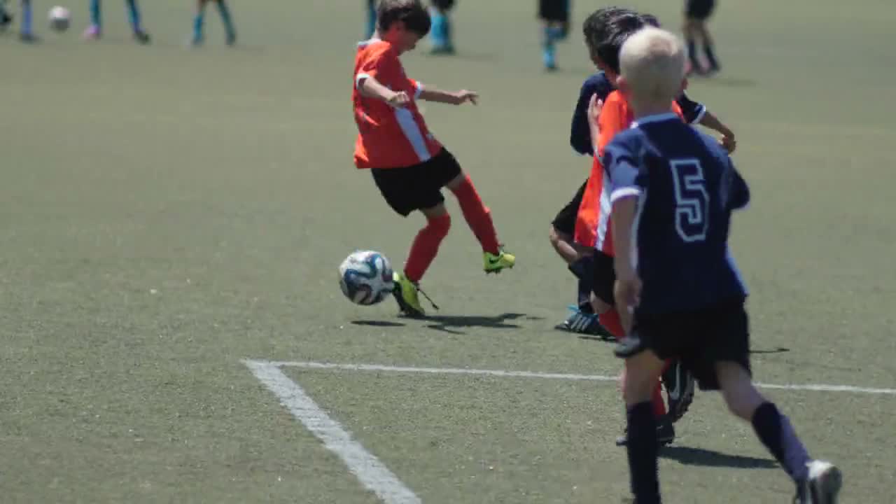 Young players chase a ball during a youth soccer game on a turf field.
