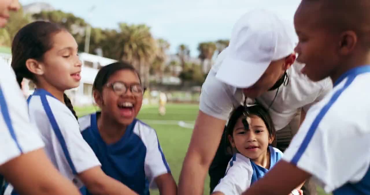 A youth soccer team and their coach put their hands in together at the start of practice.